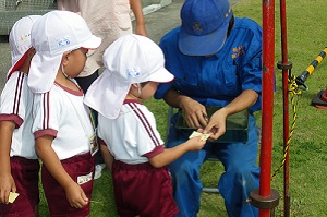 高校生のお兄さんに乗車切符を切ってもらう園児の写真